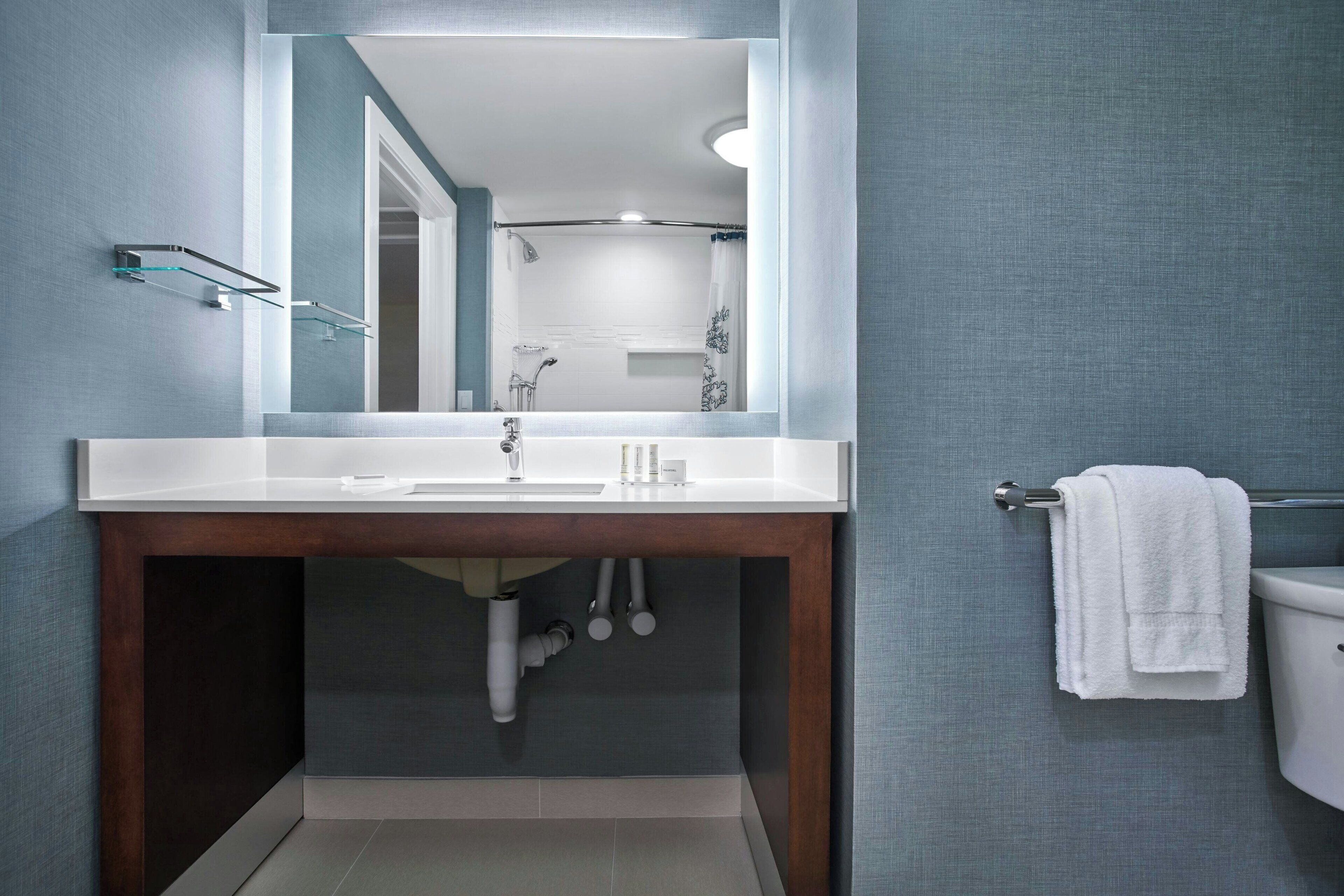 Une salle de bain moderne avec un grand miroir, un lavabo blanc et un porte-serviettes.
