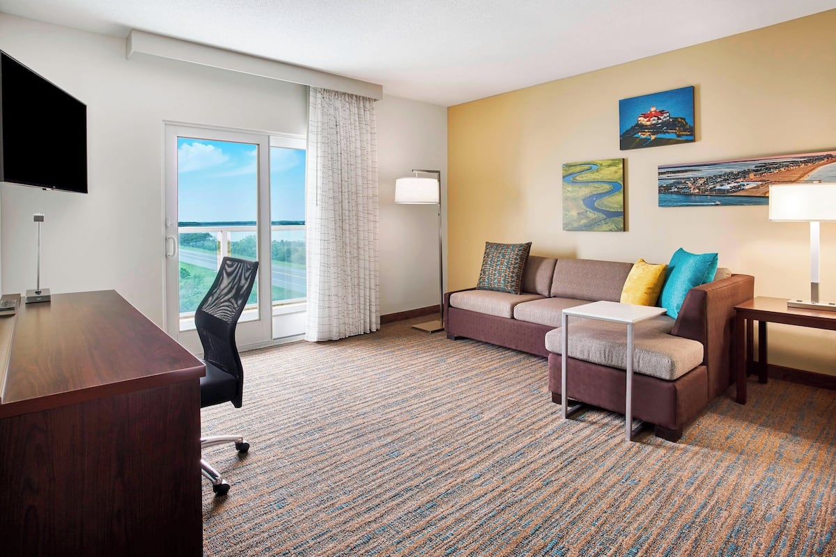 A hotel room with a large window, a sofa, a desk, and a TV.