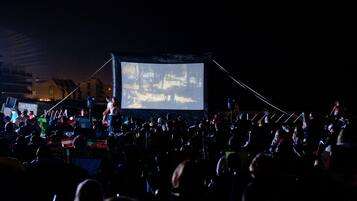 Une projection de film en plein air, avec un grand écran et des spectateurs assis en rangées.
