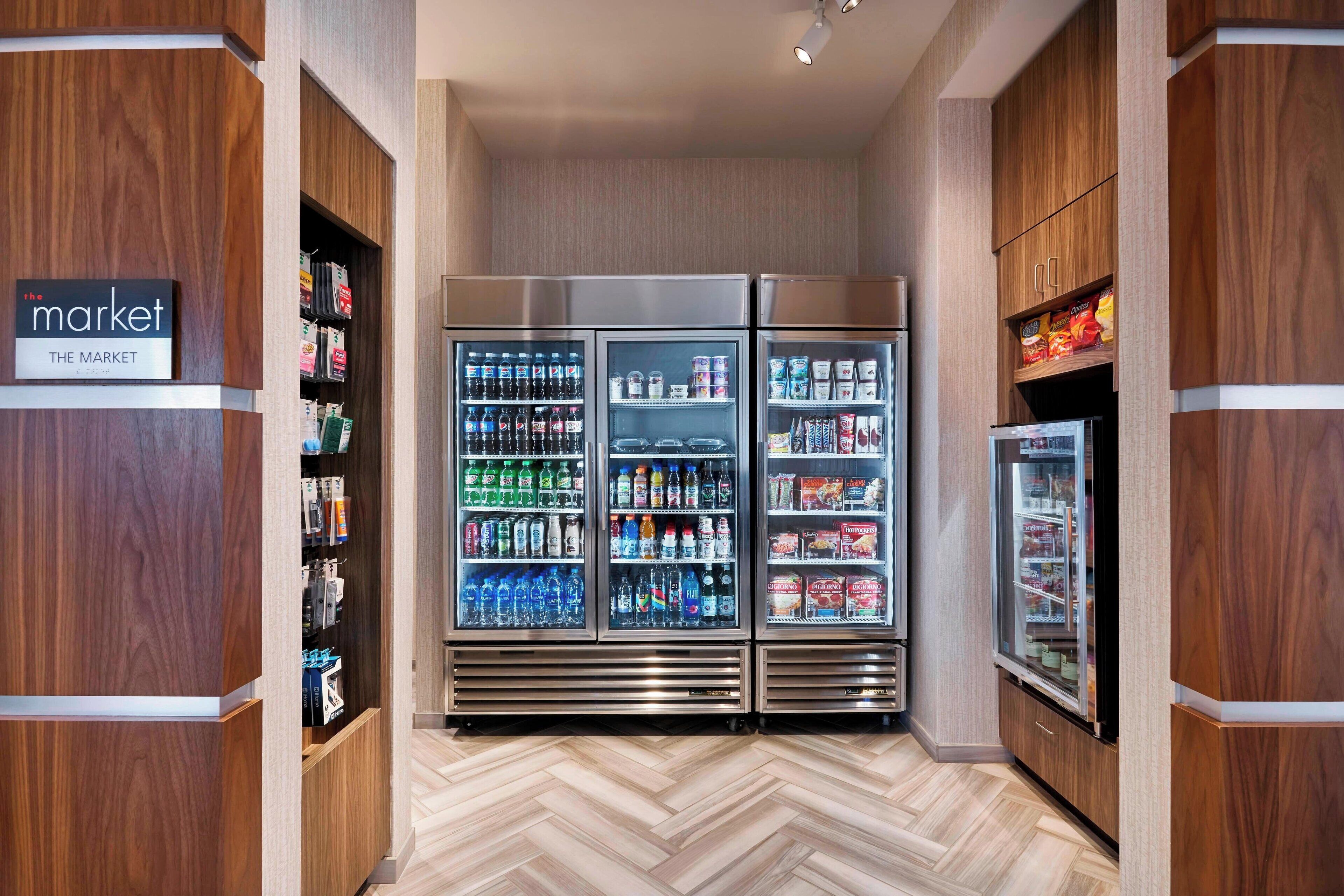 Un pasillo con paredes de madera y suelo de espiga, que conduce a un mostrador refrigerado lleno de bebidas y aperitivos.