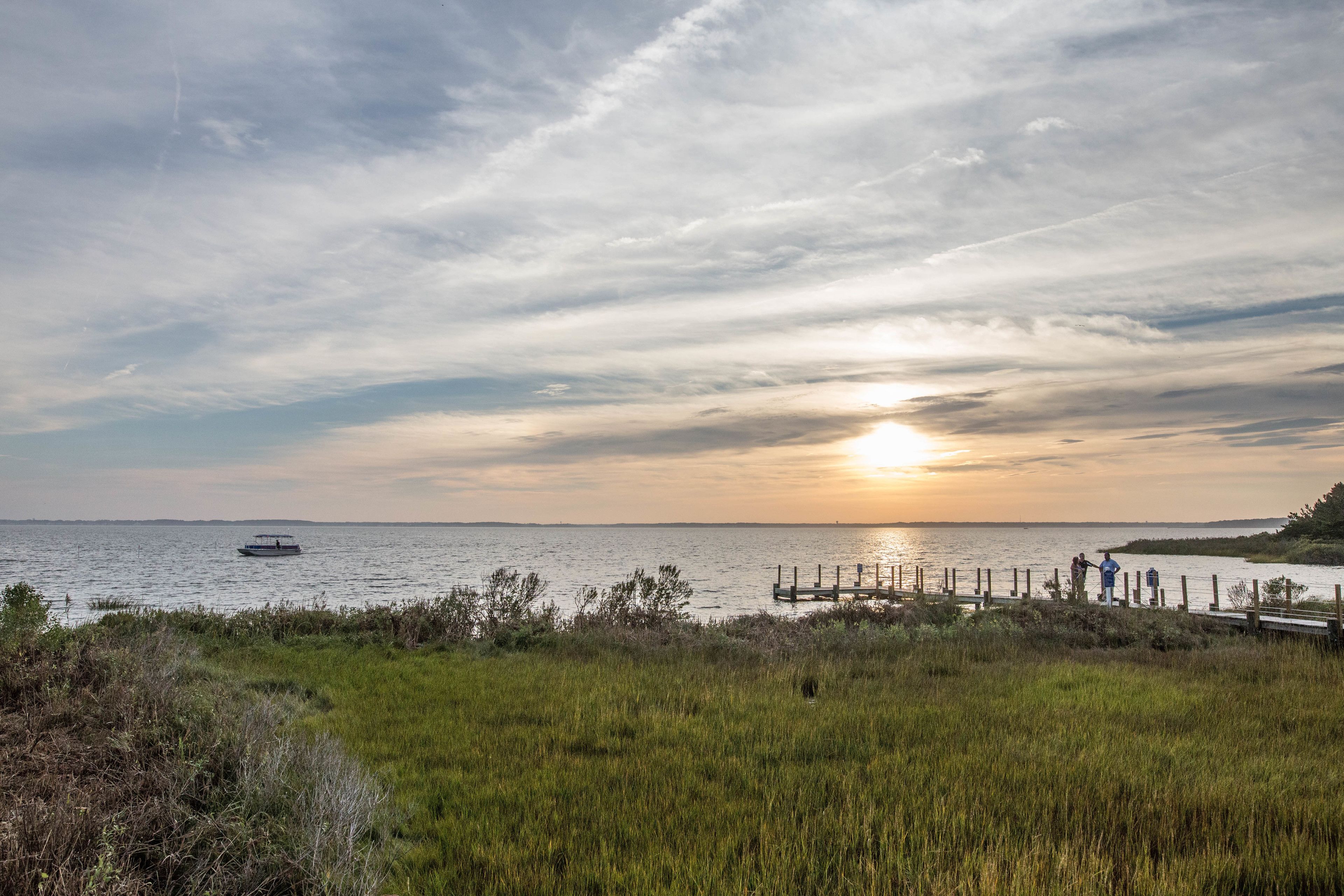 A sunset over a body of water with a boat and a dock with people.