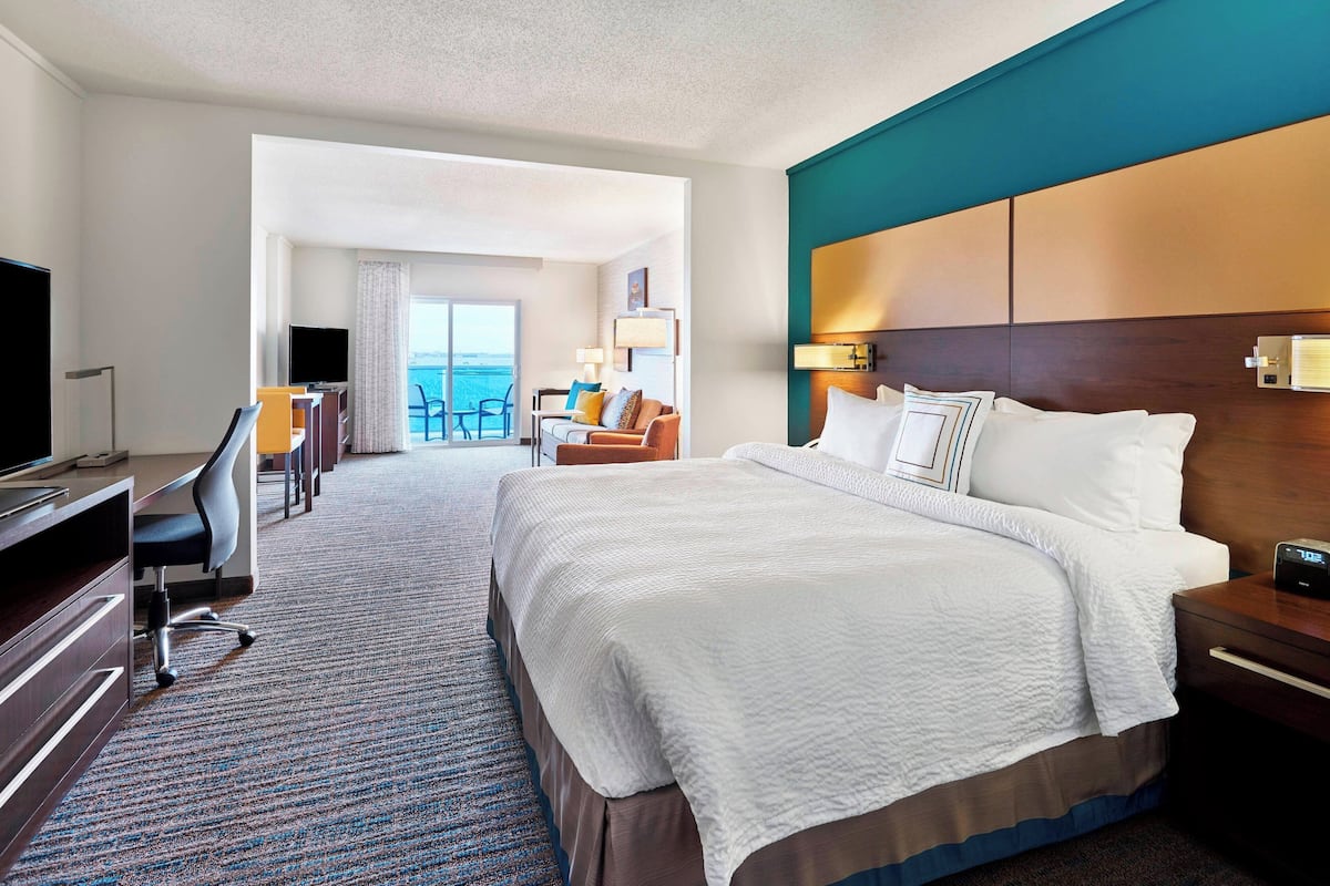 A hotel room with a large bed, a desk with a chair, a TV, and a view of the ocean.
