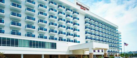 A modern hotel with a white facade, multiple balconies, and a parking lot.