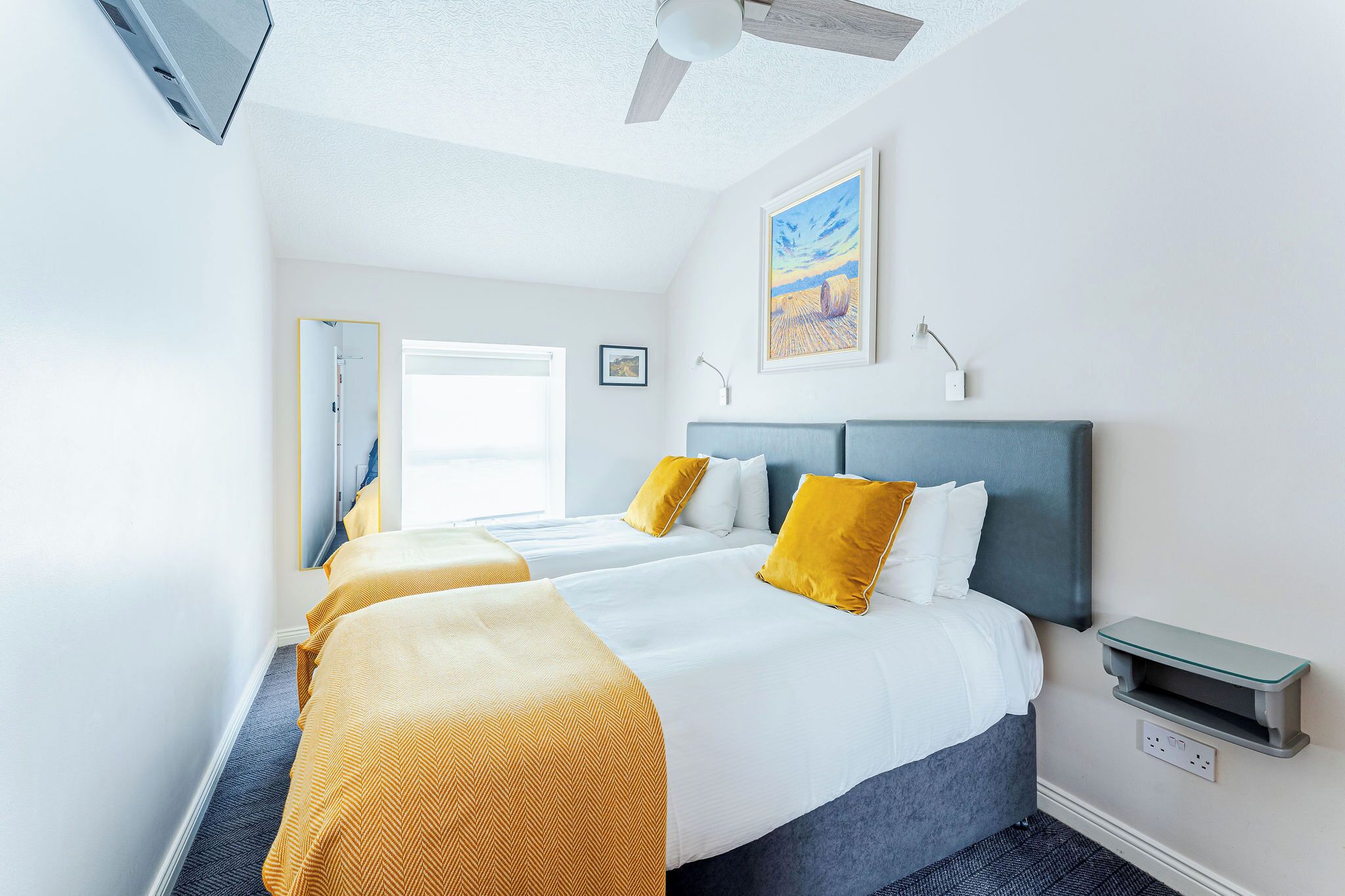 Une chambre d’hôtel avec deux lits, un ventilateur de plafond, un tableau et une table de chevet.
