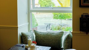 A dining area with a table set for two, a window with a view of the street, and framed pictures on the wall. - Dan Linehans Bar and B&B (Killarney)