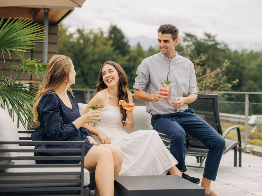 Tres personas sentadas en mobiliario exterior, disfrutando de bebidas.