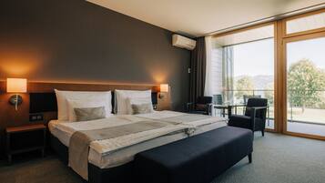 Une chambre d’hôtel avec un grand lit, des lampes de chevet, un bureau avec une chaise et une vue sur l’extérieur grâce à une grande fenêtre.