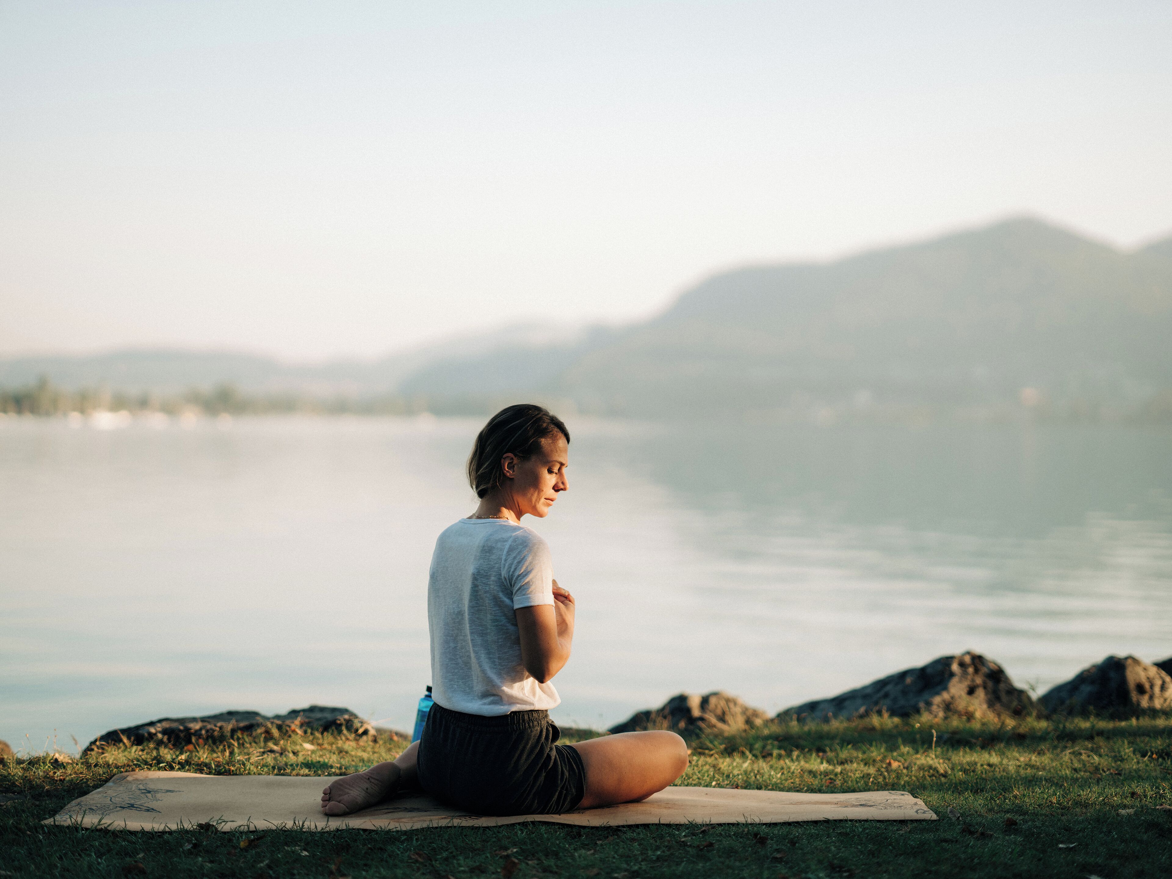 A person sitting on a mat by a lake with mountains in the background.