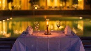 Una mesa de comedor con servilletas blancas, copas de vino y una vela, con vista a una piscina.