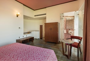 A bedroom with a bed, a wooden wardrobe, a small table, and a chair.