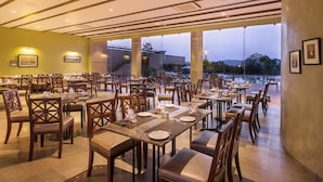 Un comedor amplio con varias mesas y sillas, ventanas grandes que ofrecen vistas al exterior y obras de arte enmarcadas en las paredes.