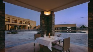 Un área de comedor al aire libre con una mesa preparada para dos personas, un pilar de piedra y un edificio al fondo.