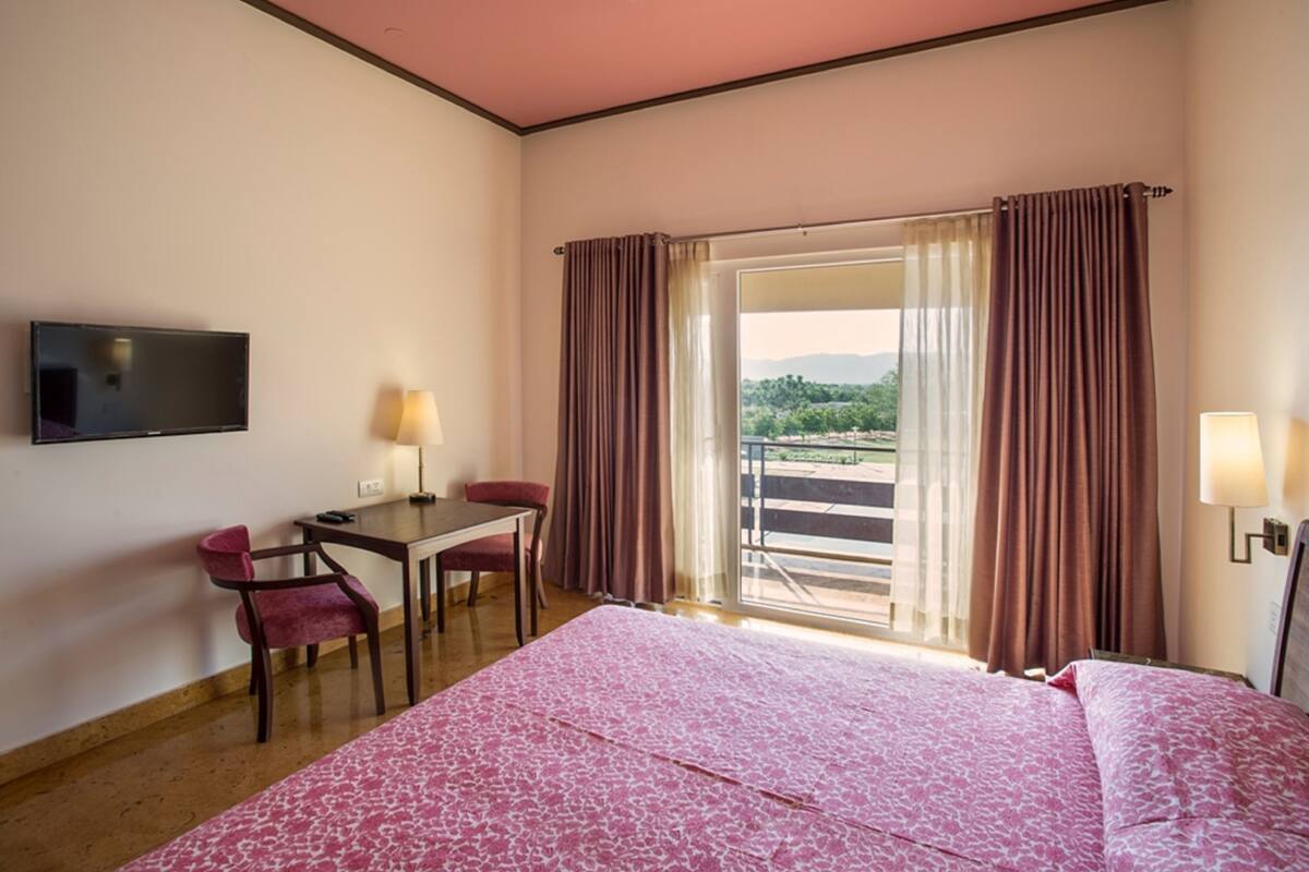 A hotel room with a bed, a desk, a chair, a TV, and a balcony with curtains.