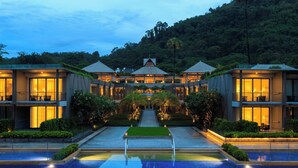 A modern hotel with a central pool, surrounded by well-maintained gardens and a mountain backdrop.