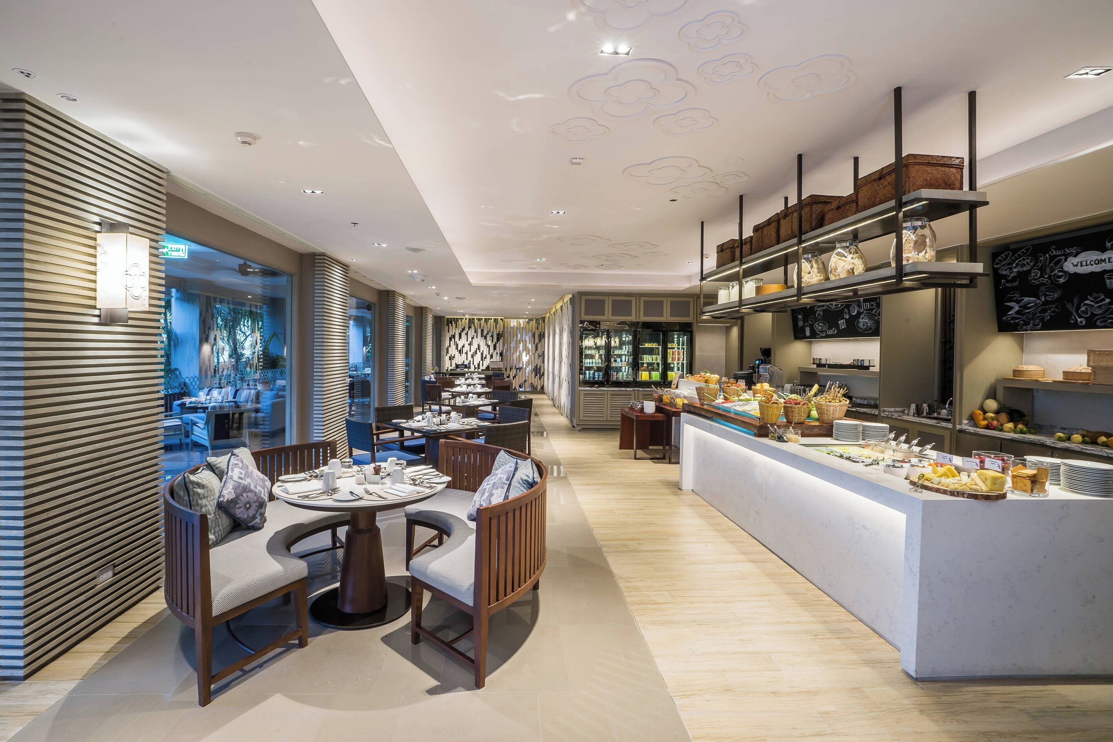 A modern restaurant with a central dining area, a buffet counter, and a view of the outdoor seating area.