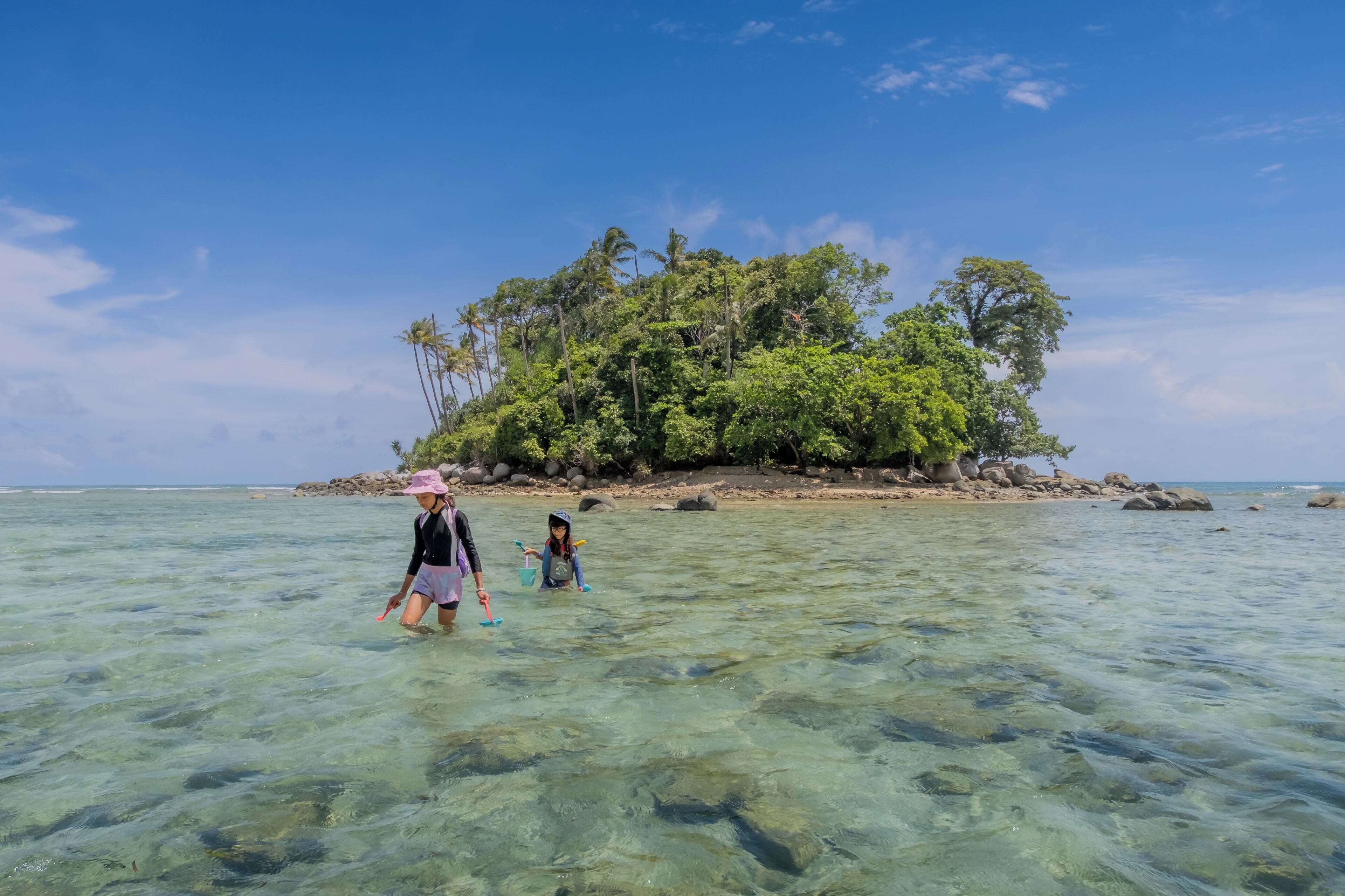A clear tropical beach with shallow water and a small island with dense vegetation in the background.