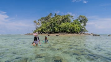 A clear tropical beach with shallow water and a small island with dense vegetation in the background.