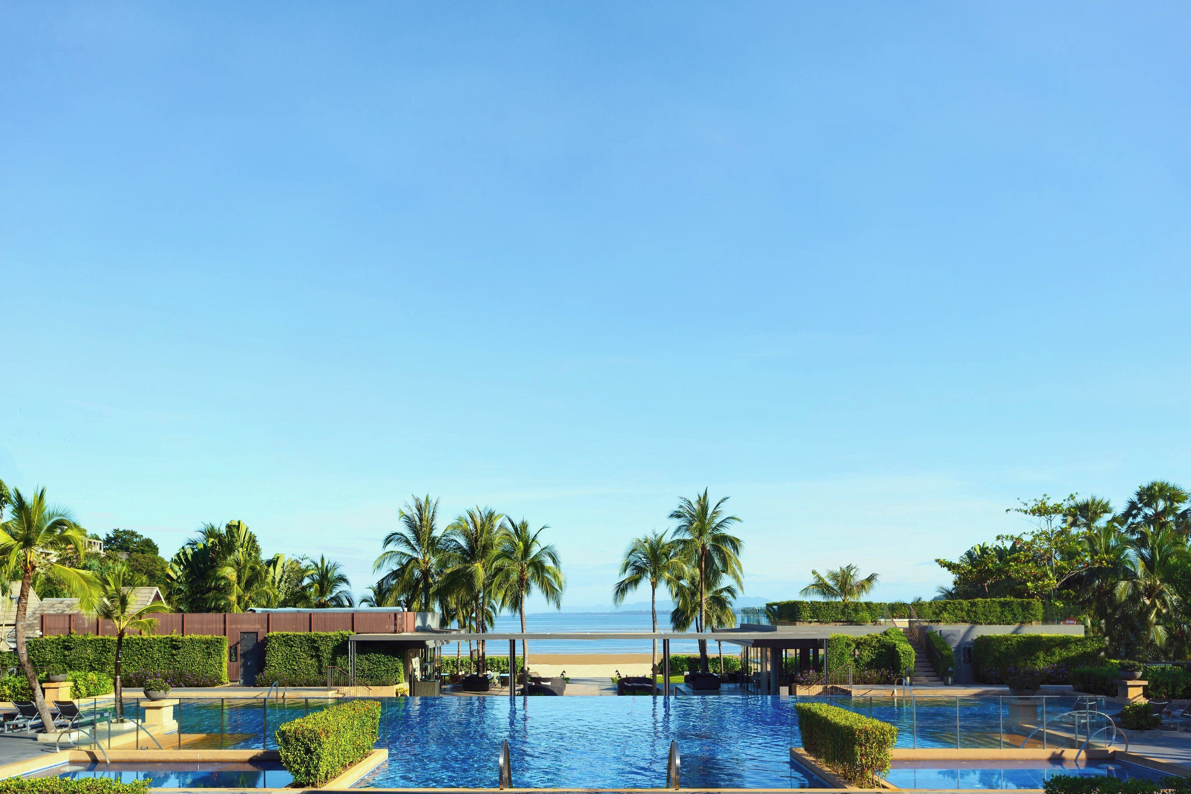 A resort pool area with multiple pools, palm trees, and a view of the beach.