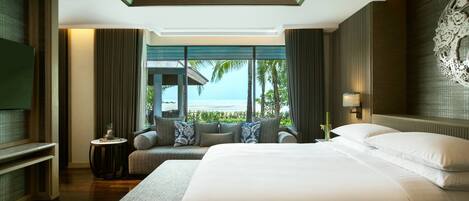 A hotel room with a large bed, a sofa, a small table, and a TV. The room has a view of the ocean.