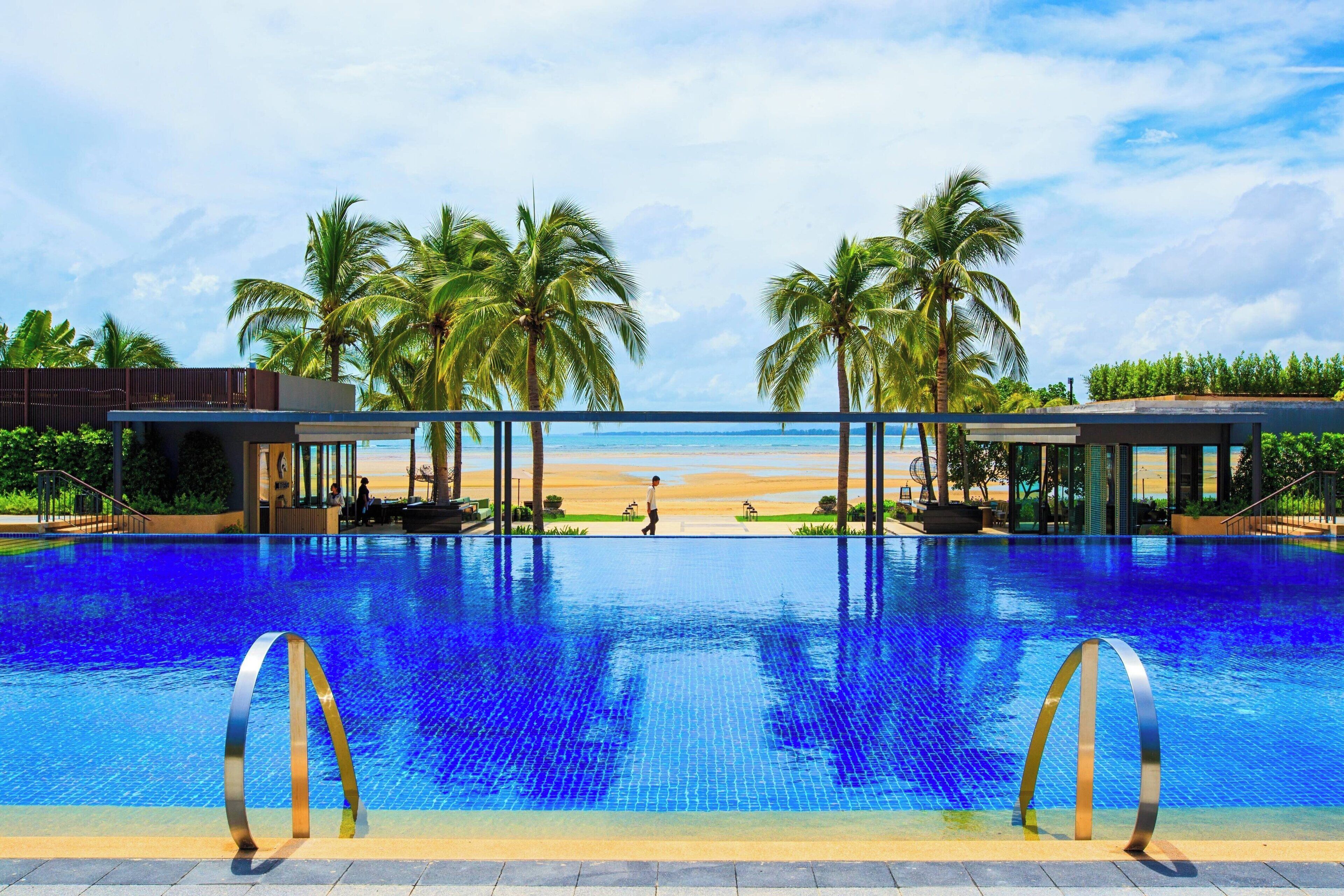 Una piscina con vista a la playa y palmeras.