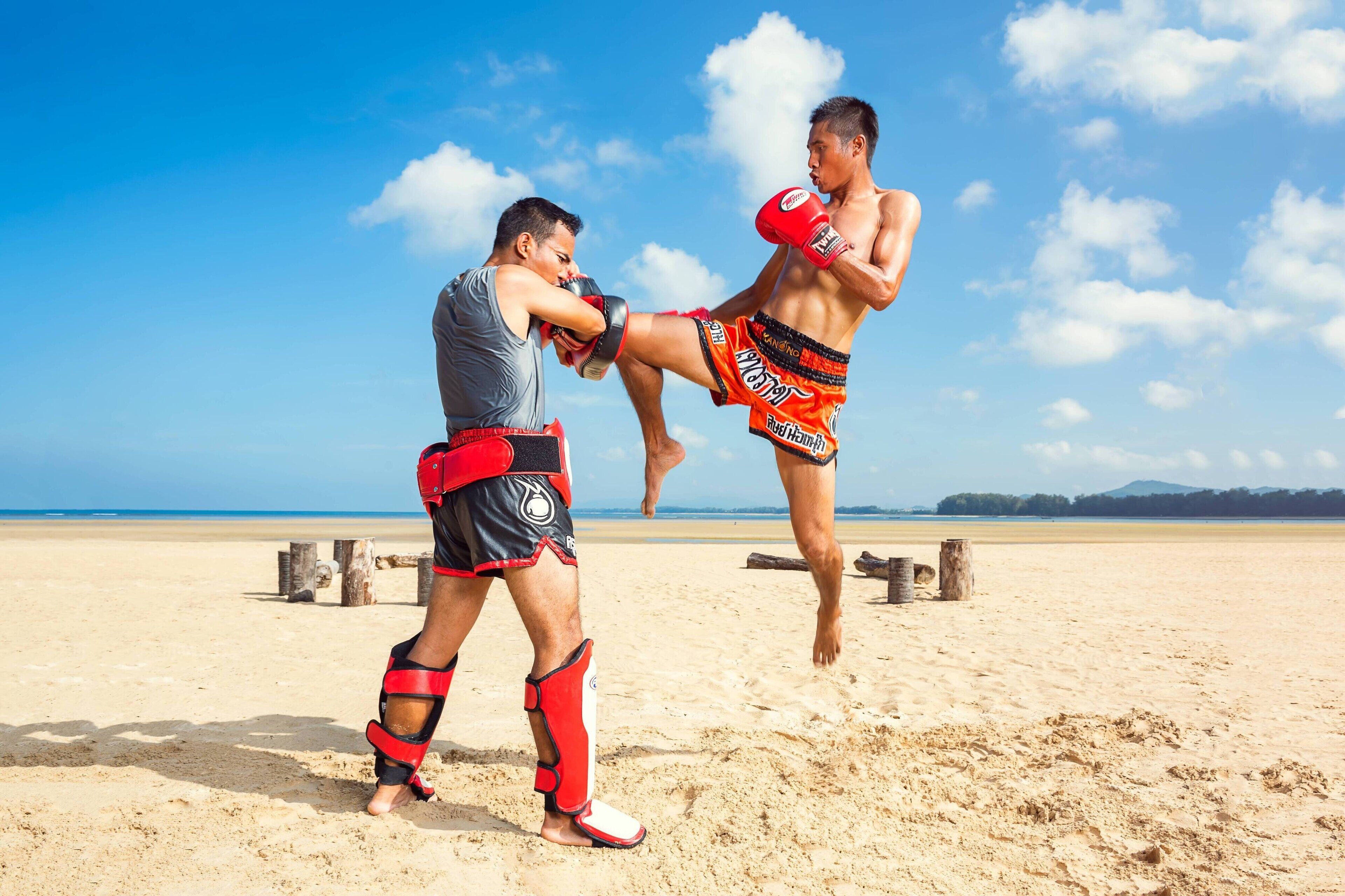 Two people practicing martial arts on a beach with a clear sky.