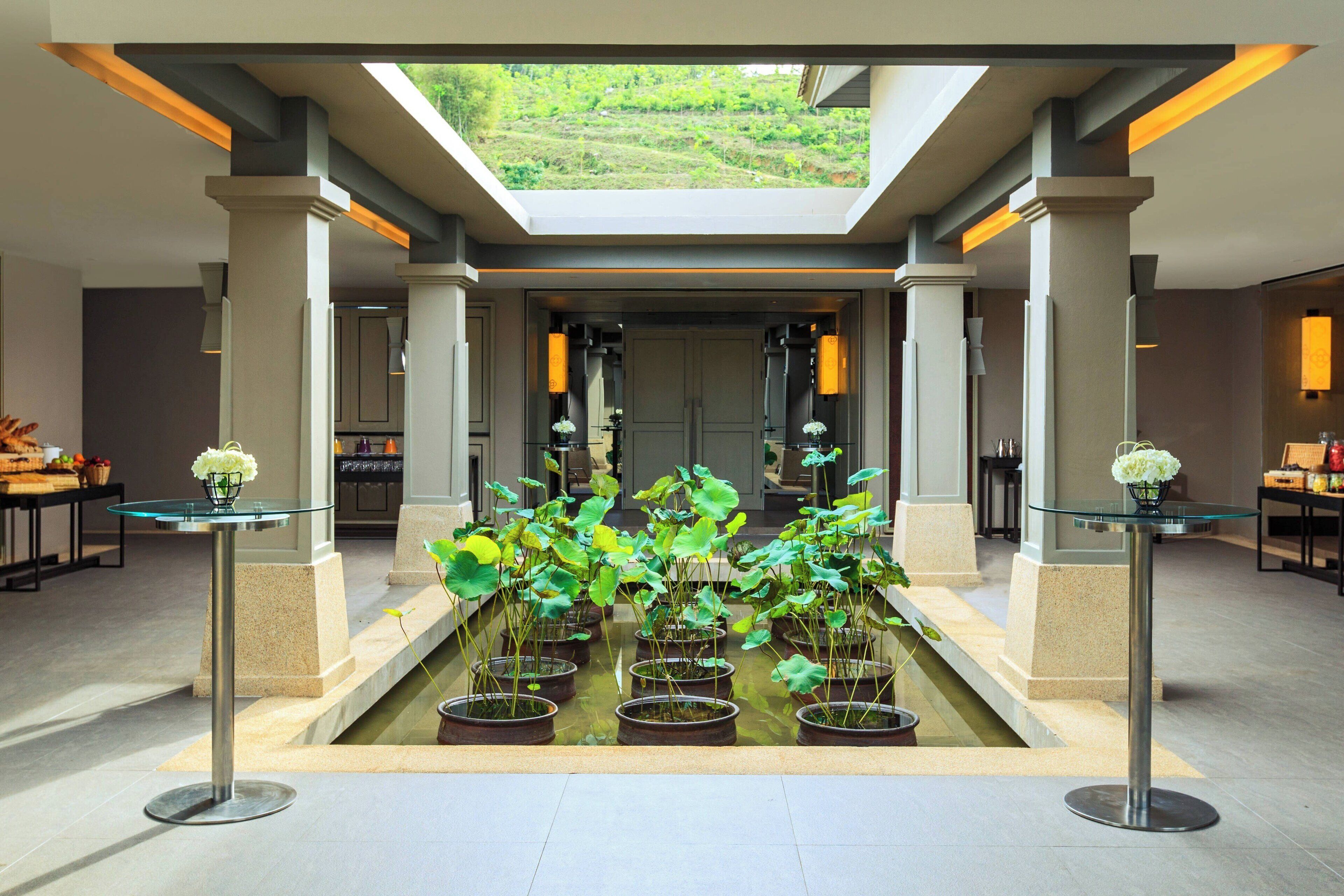 A spacious lobby with a central water feature, glass tables, and a skylight.