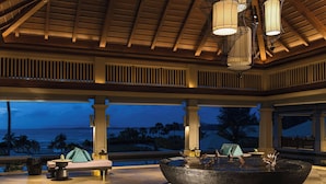 A covered outdoor area with a large water feature, seating, and a view of the ocean.