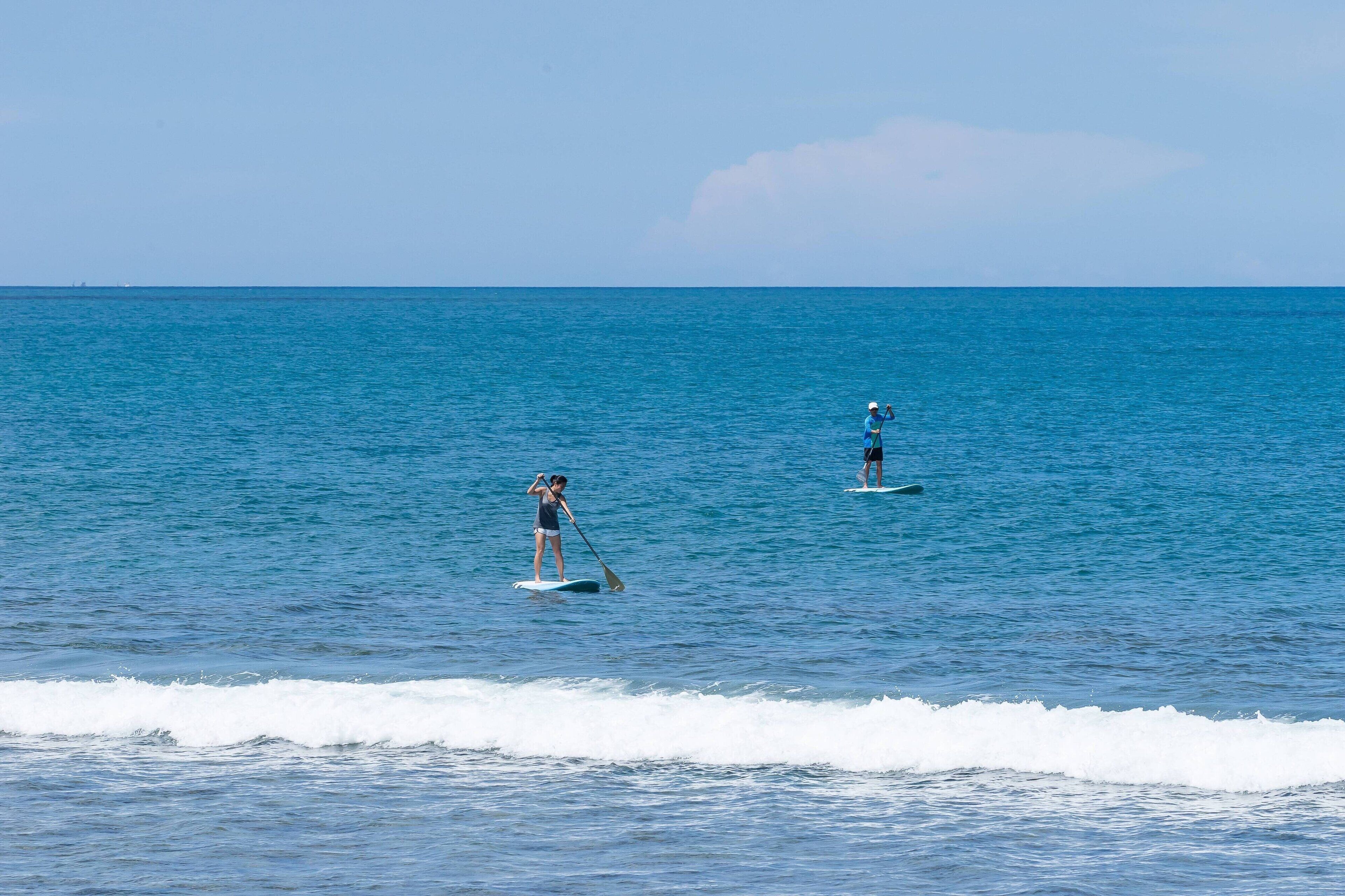 Deux personnes pratiquent le paddle sur une mer calme, sous un ciel dégagé.