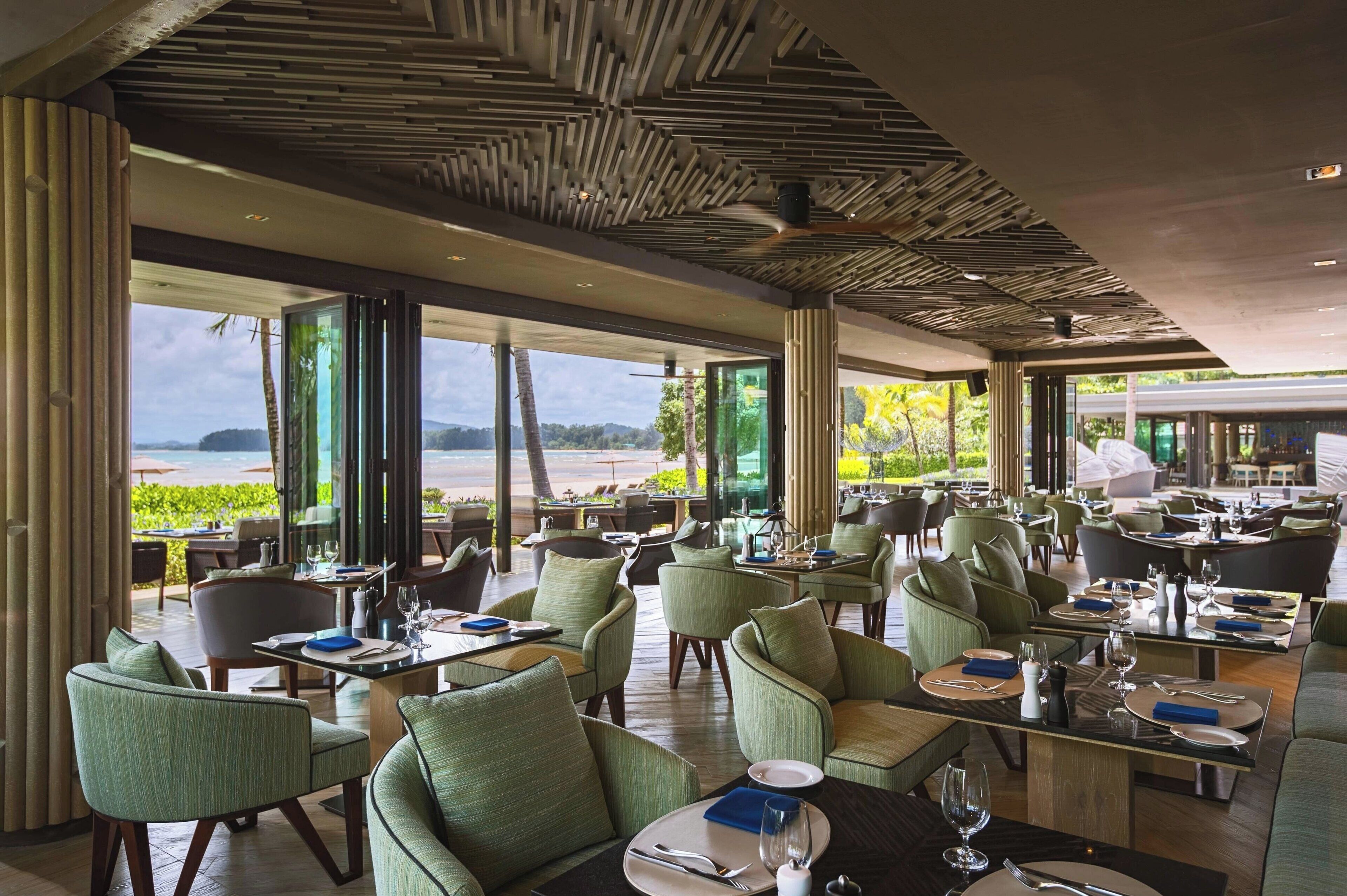 A spacious restaurant with a view of the sea, featuring modern furniture and a unique ceiling design.