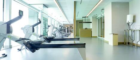 A modern gym with cardio machines, large windows, and a clean, minimalist design.
