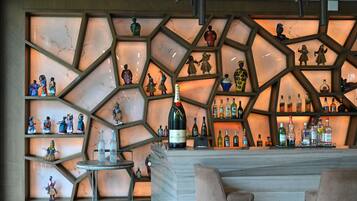 Zona de bar con mostrador de mármol, estantes con botellas y figuritas decorativas.