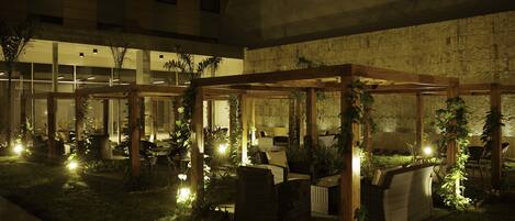 Espaço de varanda ao ar livre com móveis de vime e plantas, iluminado por iluminação ambiente.