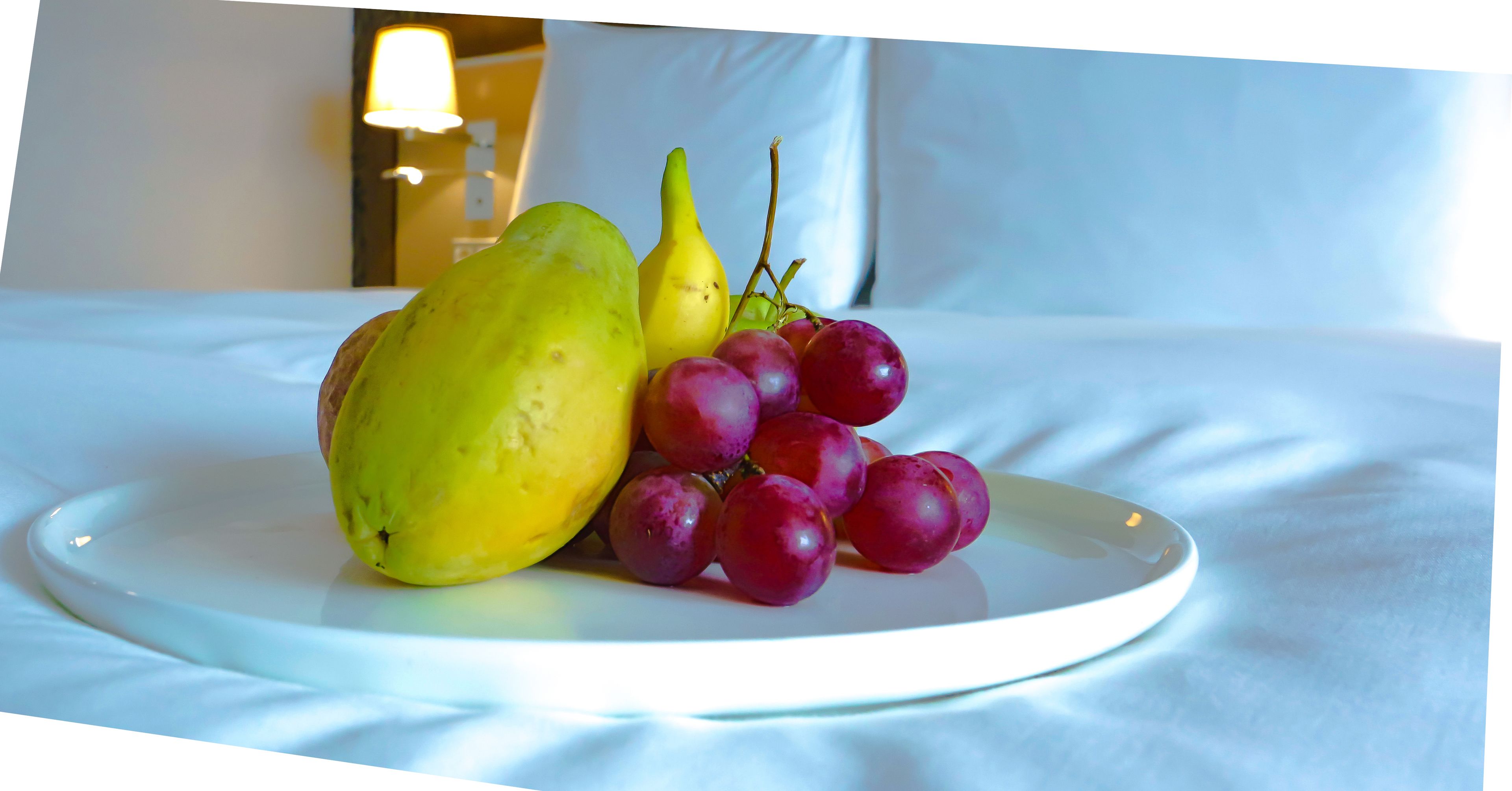 A plate with a yellow fruit, a pear, and red grapes on a bed.