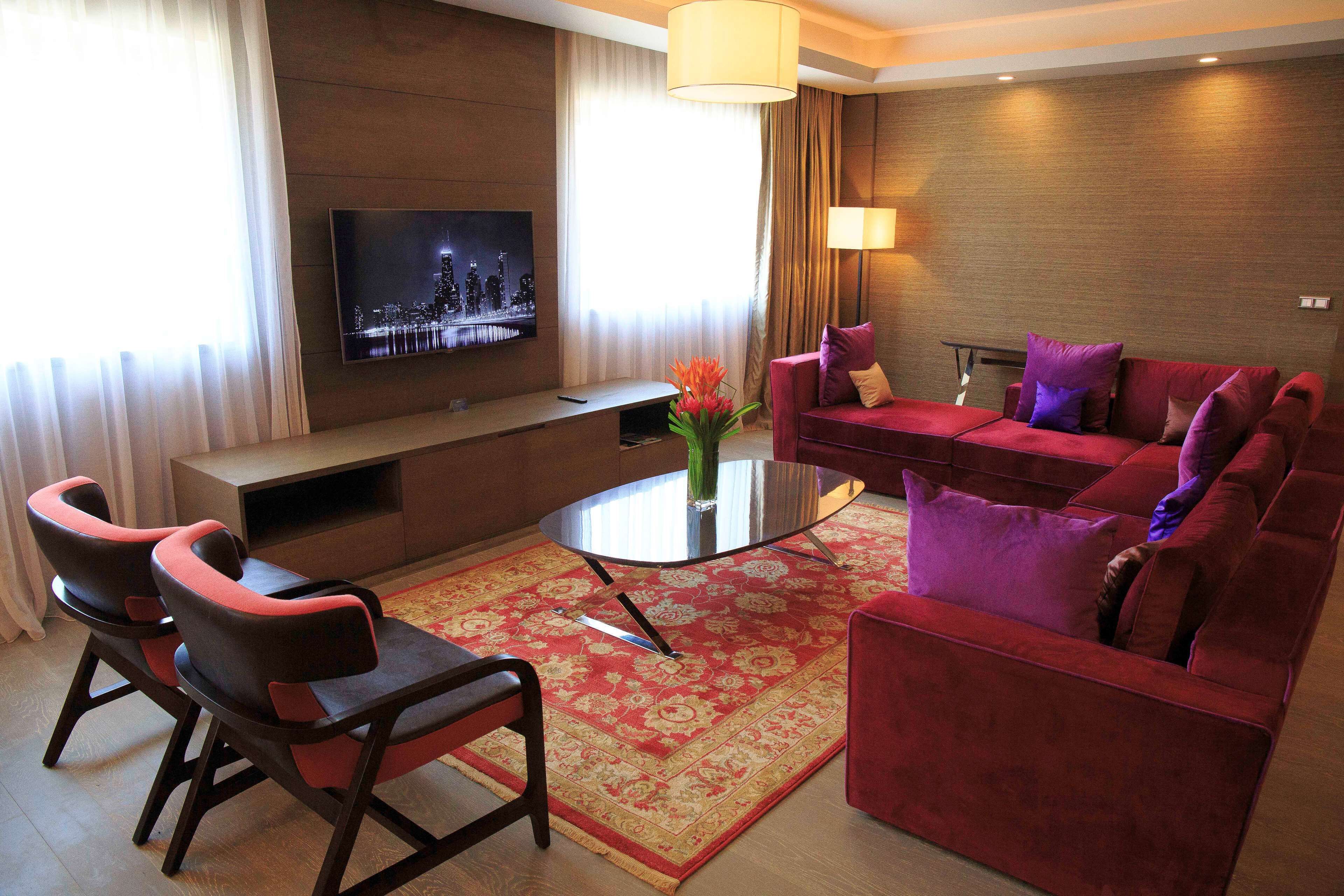 Una sala de estar moderna con un sofá rojo, dos sillones, una mesa de centro y un televisor de pantalla plana montado en la pared.