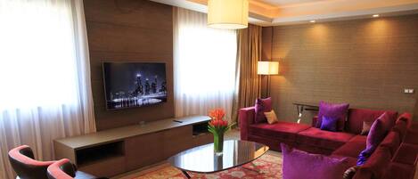Una sala de estar moderna con un sofá rojo, dos sillones, una mesa de centro y un televisor de pantalla plana montado en la pared.