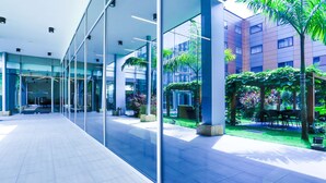 Un bâtiment moderne doté de grandes fenêtres en verre, d’un espace extérieur aménagé avec des sièges et d’un jardin bien entretenu.