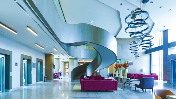 Un hall d’entrée moderne doté d’un escalier à volutes, d’espaces de détente et d’un comptoir d’accueil.