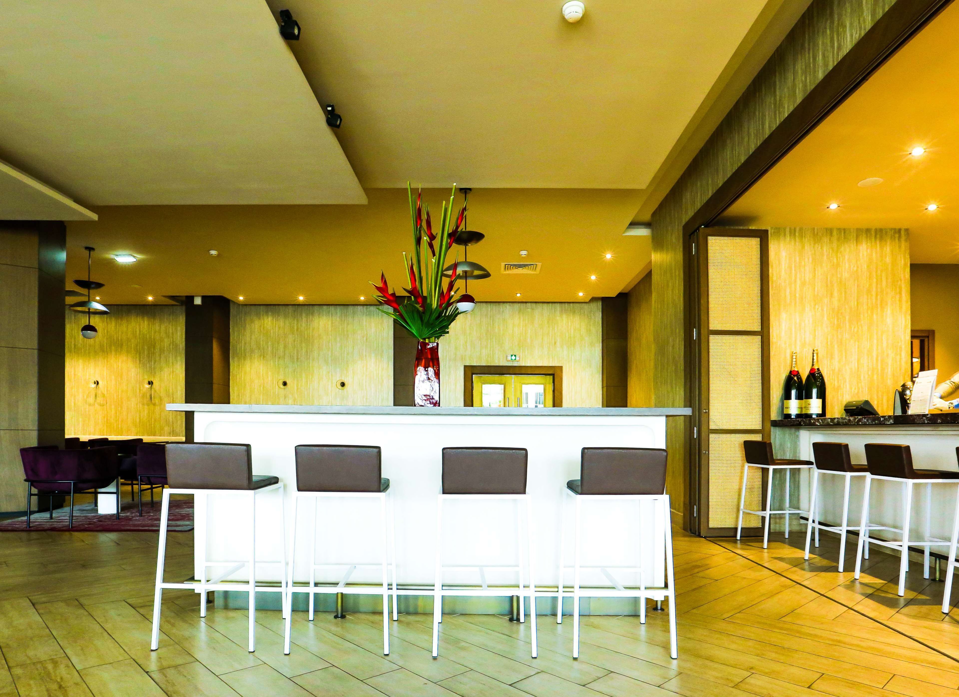 A reception area with a white counter, several bar stools, and a vase with red flowers.