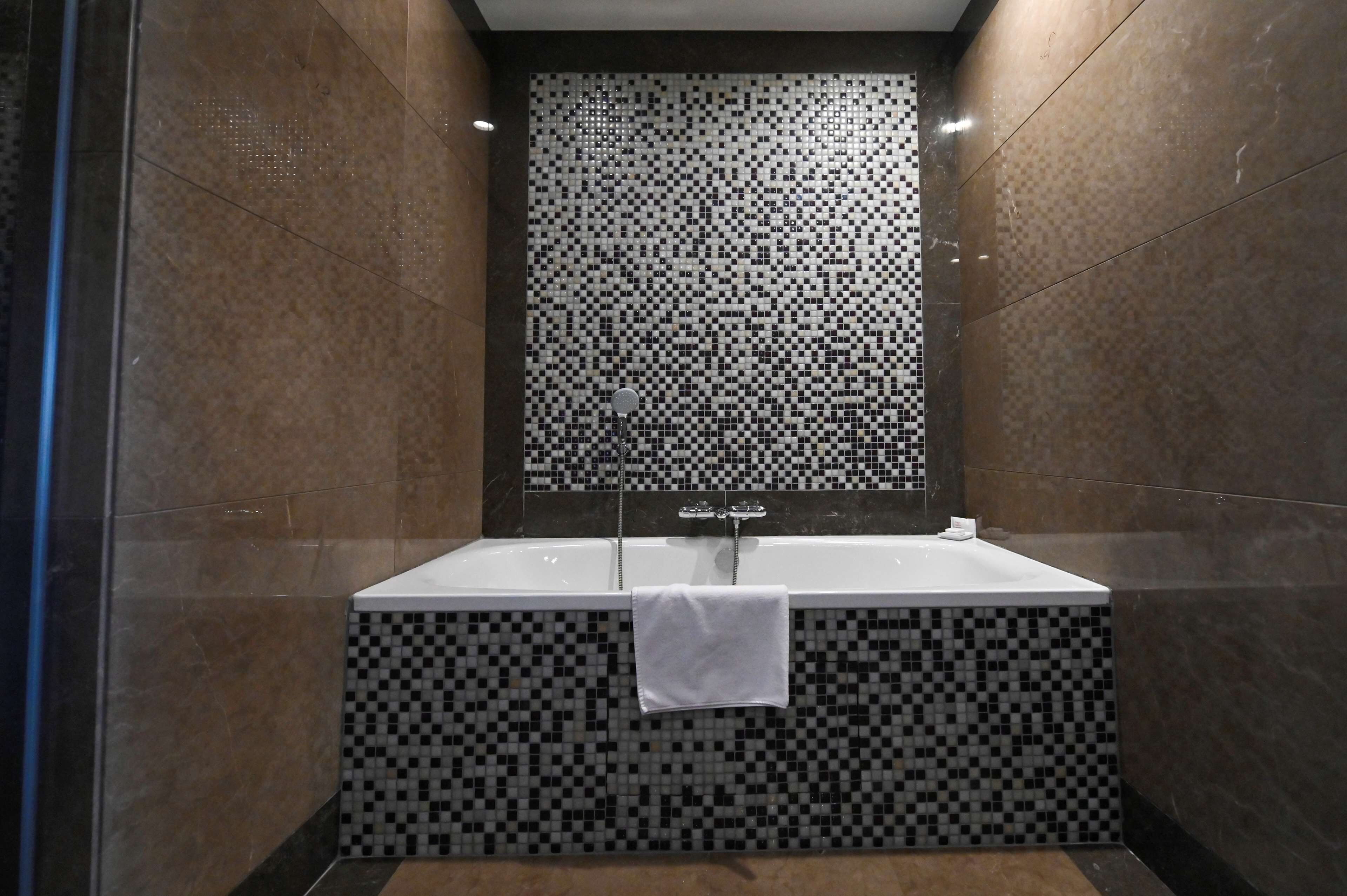 Une salle de bain moderne avec un mur recouvert d’une mosaïque à carreaux, une baignoire blanche et une douche en verre.