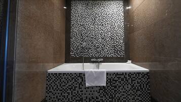 Une salle de bain moderne avec un mur recouvert d’une mosaïque à carreaux, une baignoire blanche et une douche en verre.