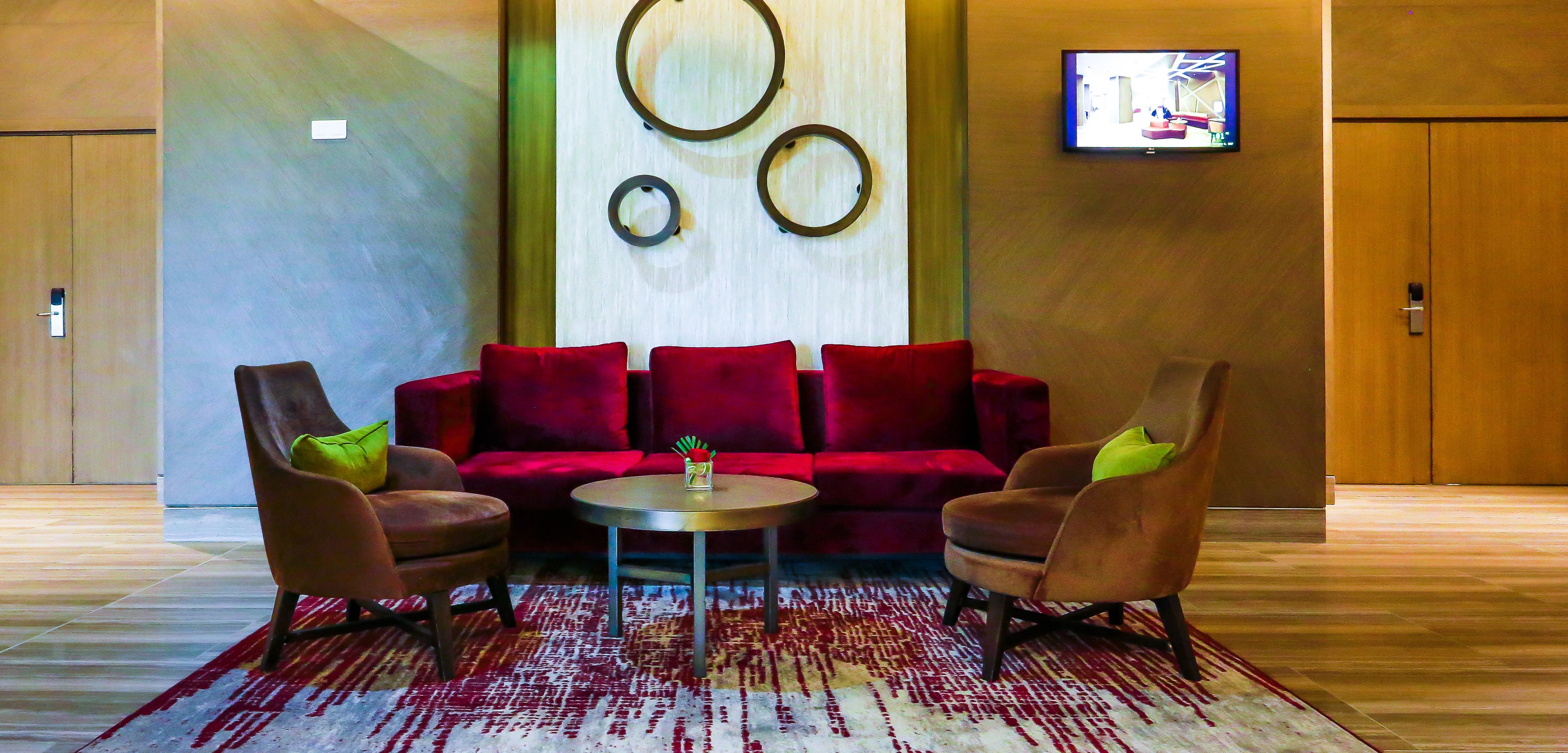 A modern lobby with a red velvet sofa, two armchairs, a small round table, and a TV mounted on the wall.