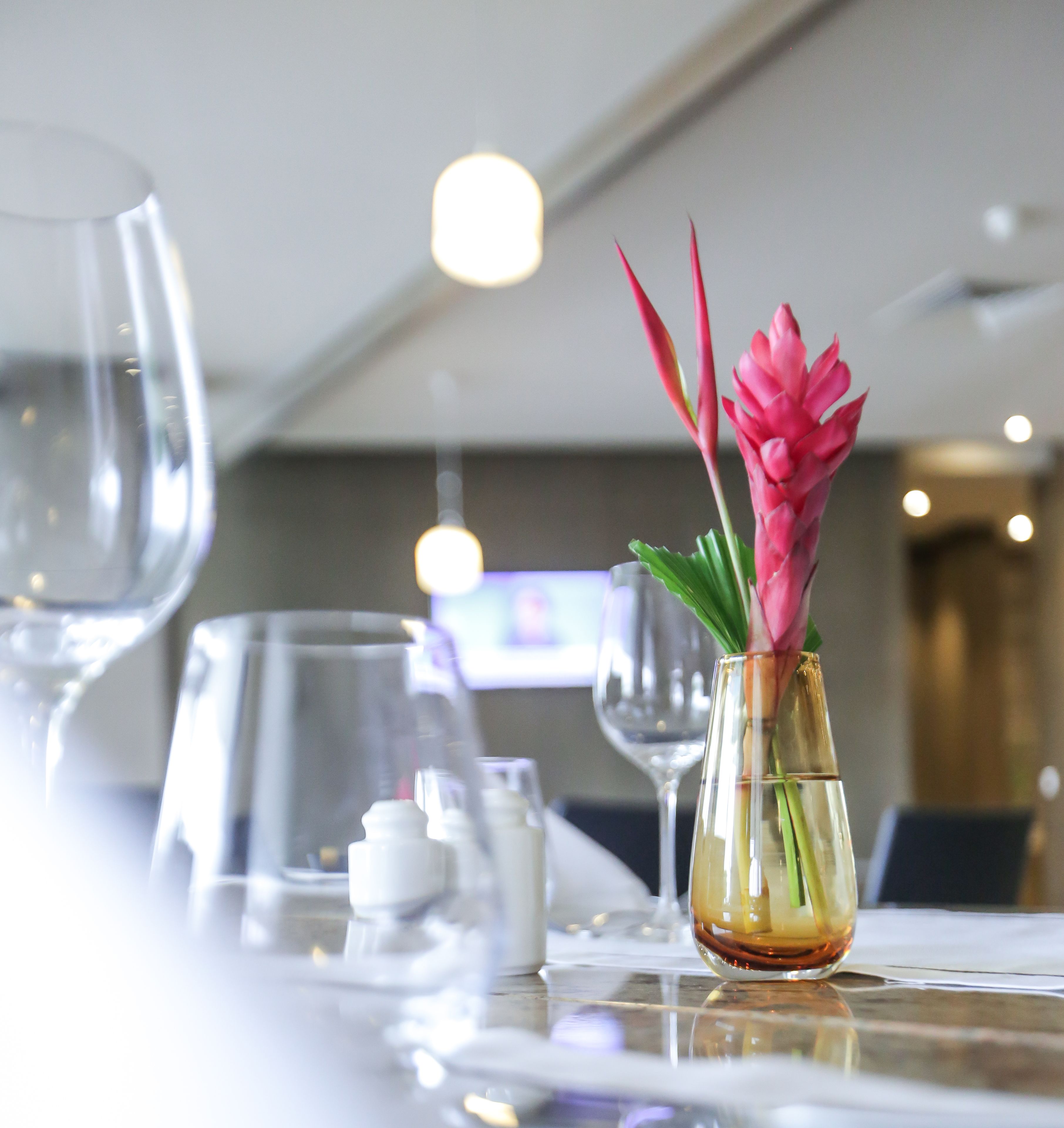 Una mesa con un florero con flores rosas, vasos transparentes y una vela.