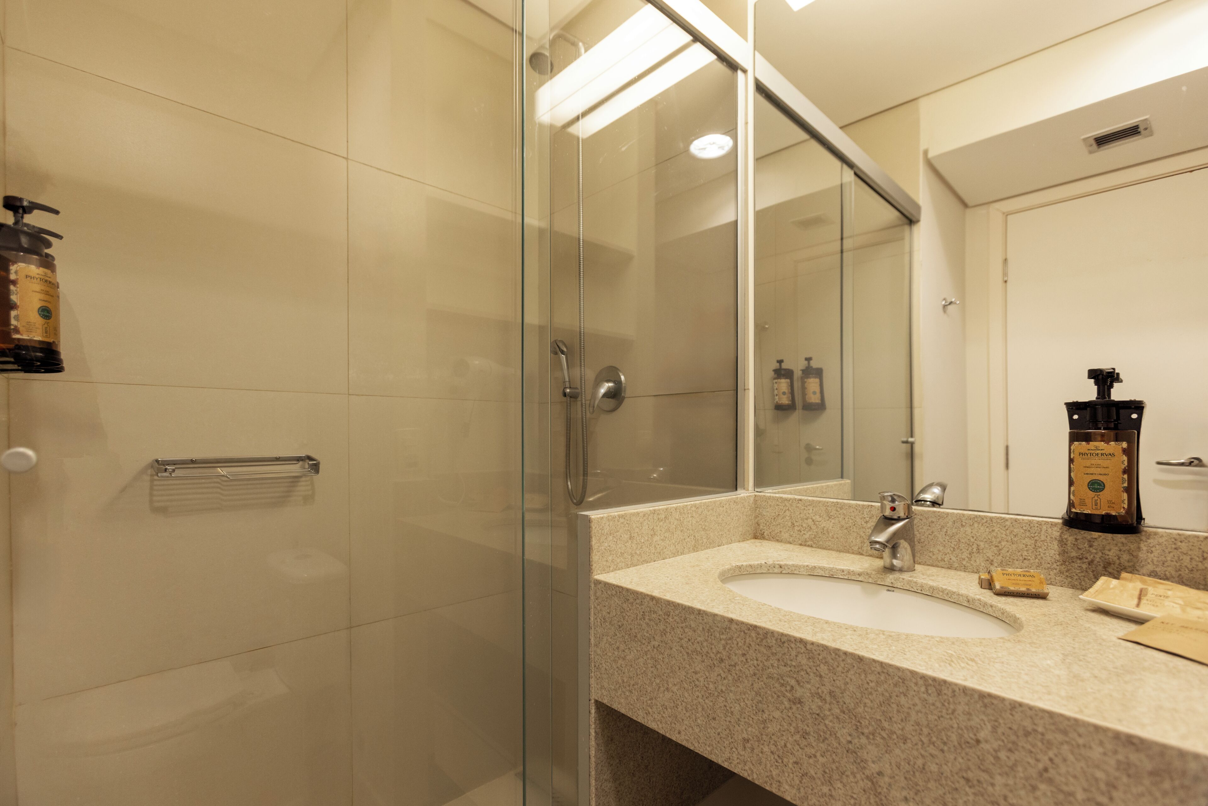 A modern bathroom with a glass shower enclosure, a granite countertop sink, and a large mirror.