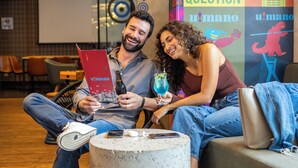 Zwei Personen sitzen auf einem Sofa mit einem Laptop und einem Getränk.