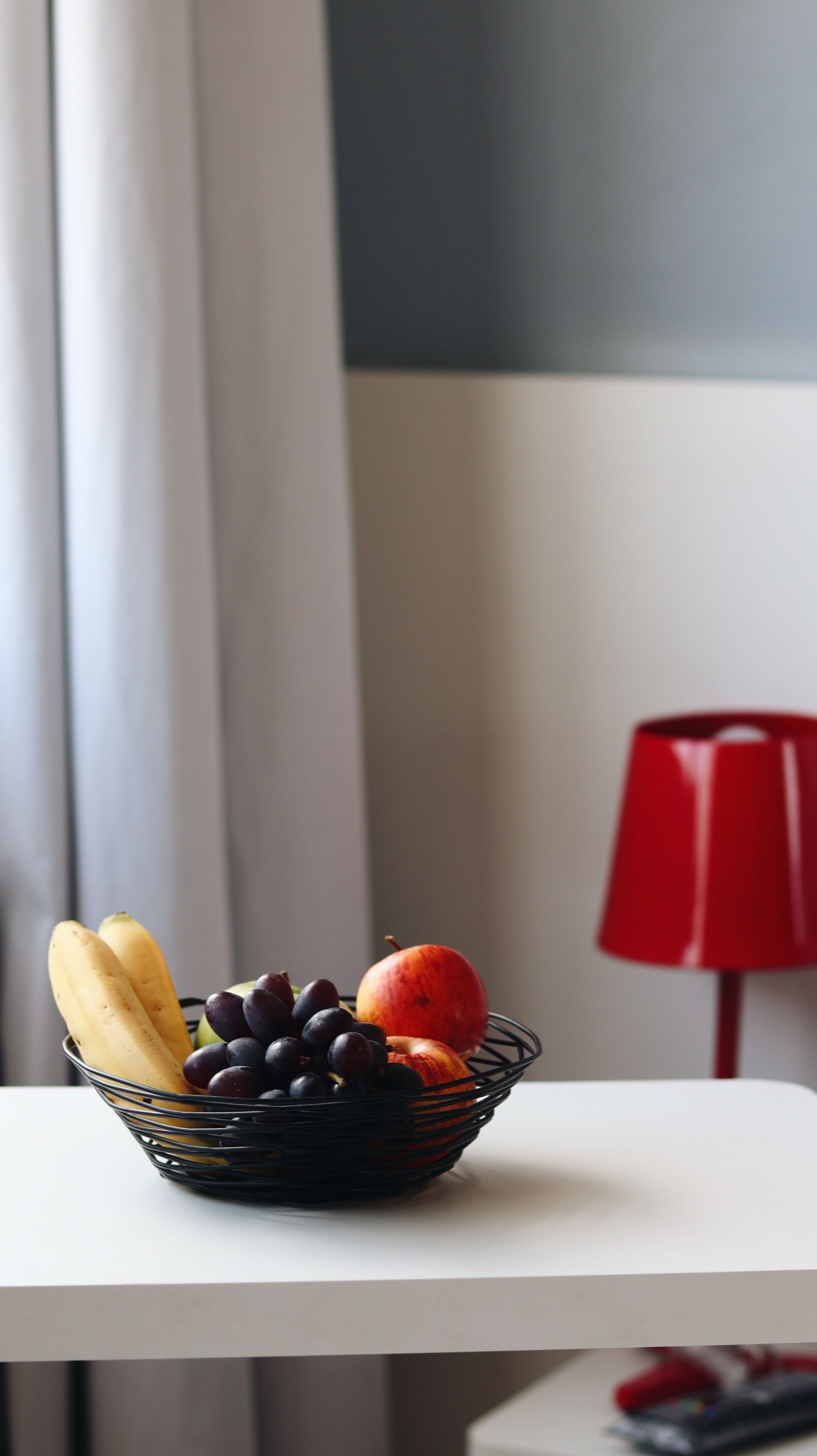 Un frutero sobre una mesa blanca, con una lámpara roja al fondo.