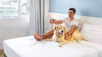 A person sitting on a bed with a dog, holding a red object.