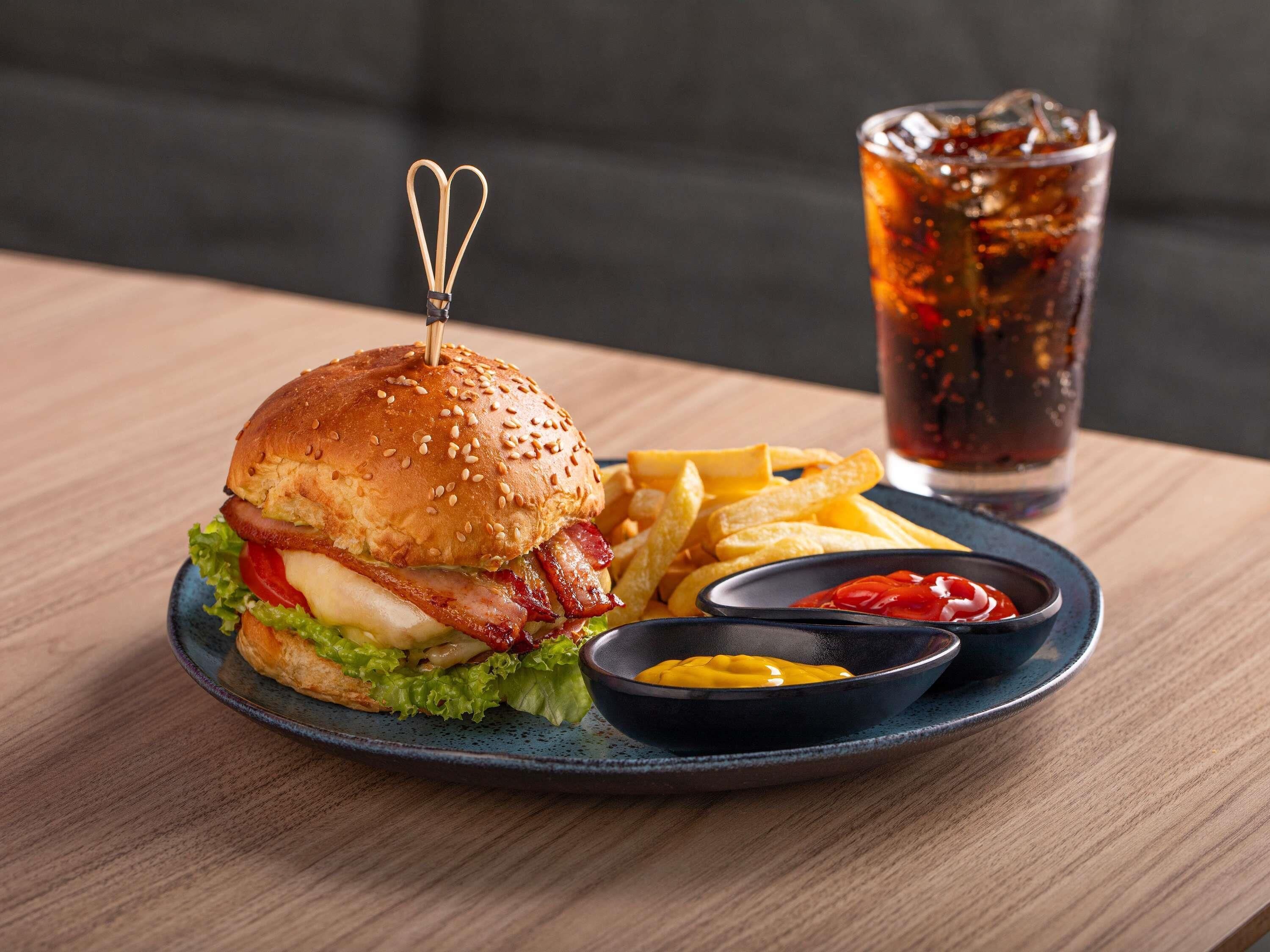 A burger with fries and ketchup on a plate, a glass of soda, and a wooden table.