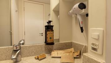 A bathroom with a sink, a hairdryer, a bottle of hand soap, and a towel dispenser.