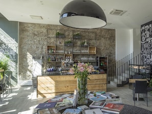 A modern bar area with a wooden counter, shelves with bottles and glasses, and a large hanging light fixture.