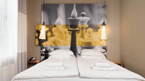 A hotel room with a large bed, two bedside lamps, a telephone, and a painting on the wall.